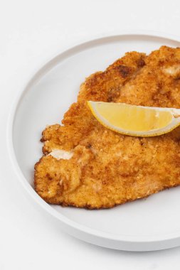 Beyaz bir arka plan üzerinde bir tabakta limon ile ekmekli ve kızarmış tavuk eti