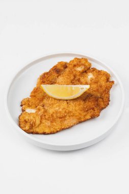 Beyaz bir arka plan üzerinde bir tabakta limon ile ekmekli ve kızarmış tavuk eti