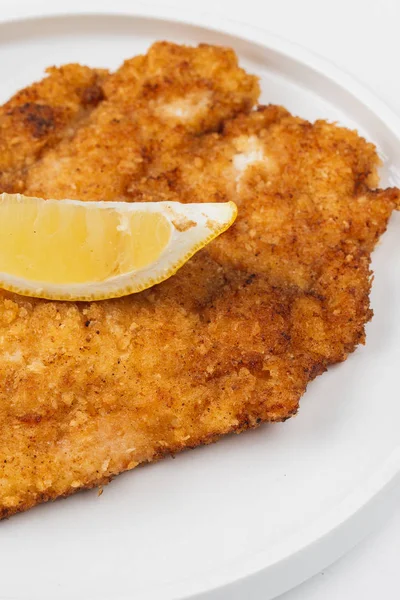 Beyaz bir arka plan üzerinde bir tabakta limon ile ekmekli ve kızarmış tavuk eti