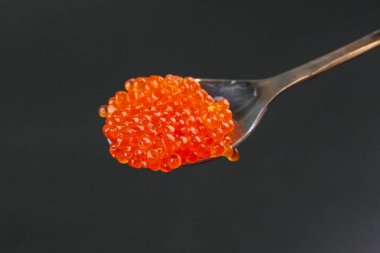 Kaşık içinde kırmızı tuzlu havyar siyah arkaplanda izole edilmiş.