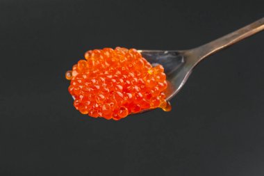 Kaşık içinde kırmızı tuzlu havyar siyah arkaplanda izole edilmiş.