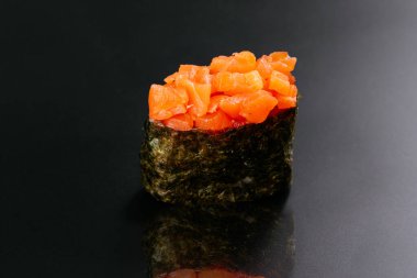 Kırmızı somonlu suşi rulosu ve siyah nori siyah masa arkasında izole edilmiş.