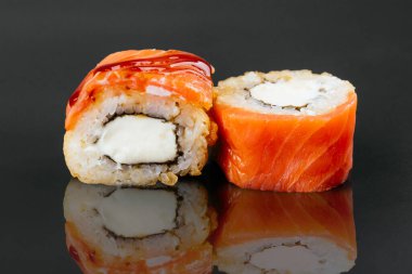 Somon balıklı suşi ruloları ve siyah masa arkasına izole edilmiş krem peynirli pirinç.