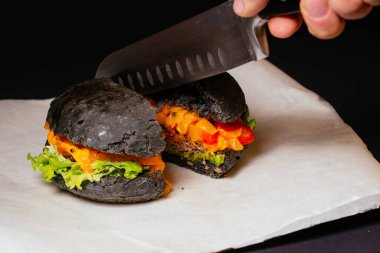 Peynirli, domatesli ve ahşap masadaki yarım siyah et burgerini dilimliyorum. 