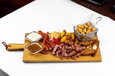 Beyaz masadaki ahşap tahtada soslu tuzlu atıştırmalıklar.