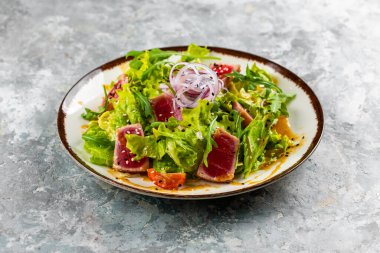 yeşil salata tabağı ile ton balığı dilimleri, domatesler ve soğanlar gri masa arkasında