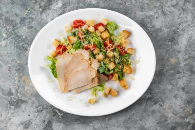 Gri arka planda beyaz tabaktaki et dilimleri ile Cezar salatasının yakın görüntüsü