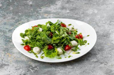 Yakın çekim, mozarella soslu yeşil salata ve gri arka planda domatesler.