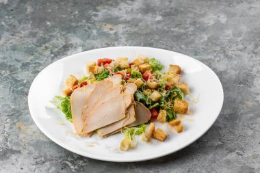 Gri arka planda beyaz tabaktaki et dilimleri ile Cezar salatasının yakın görüntüsü