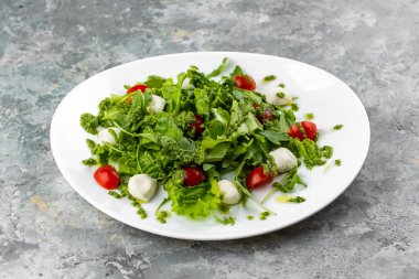 Yakın çekim, mozarella soslu yeşil salata ve gri arka planda domatesler.