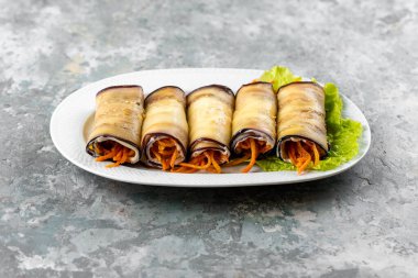 Havuçlu patlıcan ruloları ve beyaz tabakta yeşil salata.