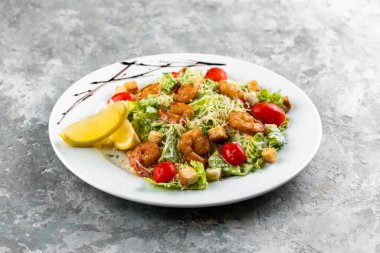 Yeşil sebzeli Cezar salatası ve beyaz tabakta karides.
