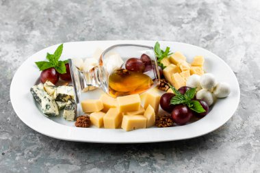 Beyaz masada beyaz bal bardağıyla servis edilen fındık üzümlü peynir tabağı.