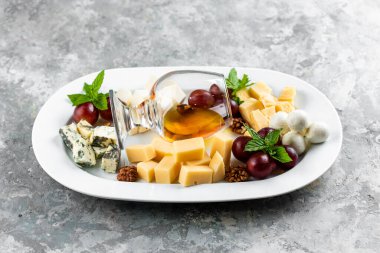 Beyaz masada beyaz bal bardağıyla servis edilen fındık üzümlü peynir tabağı.