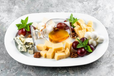 Beyaz masada beyaz bal bardağıyla servis edilen fındık üzümlü peynir tabağı.