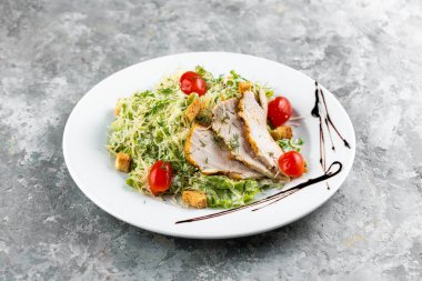 Yeşil sebzeli Cezar salatası ve beyaz tabakta tavuk dilimleri.