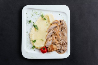 Patates püresi dilimlenmiş et ve beyaz tabakta domates.