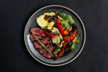 Izgara sebzeler ve siyah tabakta ızgara et. 