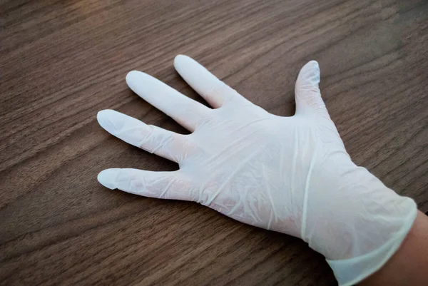 Masanın üzerindeki plastik eldivenli bir elin görüntüsü. Tek kullanımlık lateks lastik eldivenler. Covid-19 virüsüne karşı koruma önlemleri. Dezenfeksiyon ve Cerrahi Eldiven
