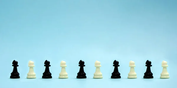 Satranç taşları, siyah ve beyaz piyonlar mavi arka planda sıralanır..
