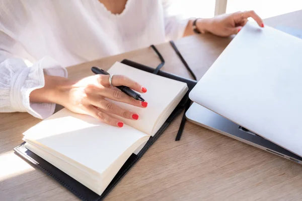 Elegant woman holds a pen with her hand in a notebook while opening her laptop. Copy space. Business and young entrepreneurs concept