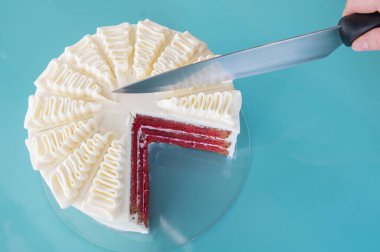 Büyük bıçaklı bir kadın eli turkuaz arka planda lezzetli bir pasta kesiyor.