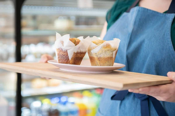A coffee shop woman owner carrying a plate with two appetizing muffins.Copy space.Delicious moments. Small business concept.