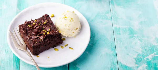 Chocolate brownie, cake on a white plate on a turquoise wooden background. Copy space.
