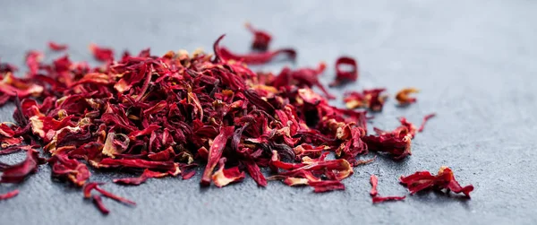 Hibiscus flower tea scattered on grey stone background. Copy space.