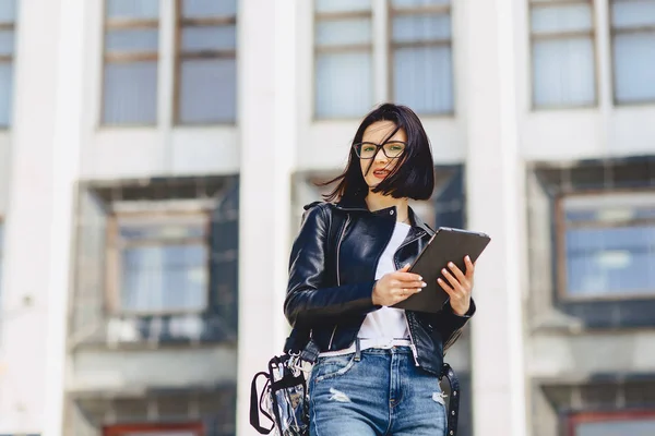 attractive girl in glasses with tablet on background of building outside