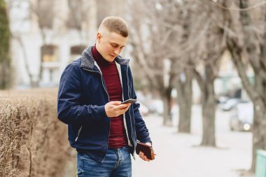 Sokak ortasında telefon ile basit ceketli çocuk duruyor
