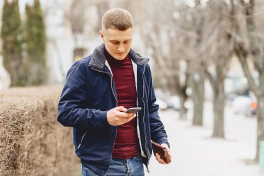 Sokak ortasında telefon ile basit ceketli çocuk duruyor