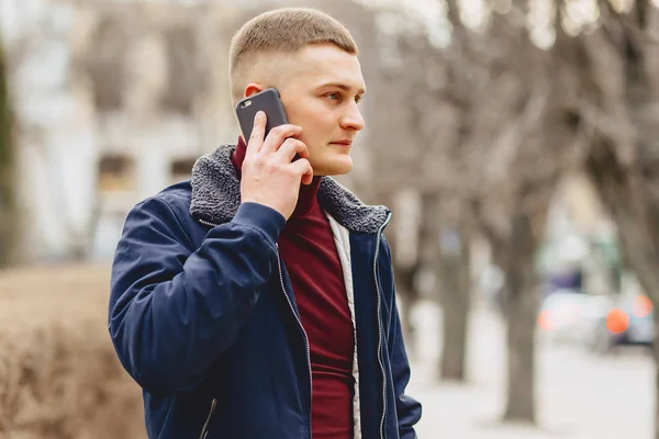 Guy in jacket simple stands with phone in middle of alley