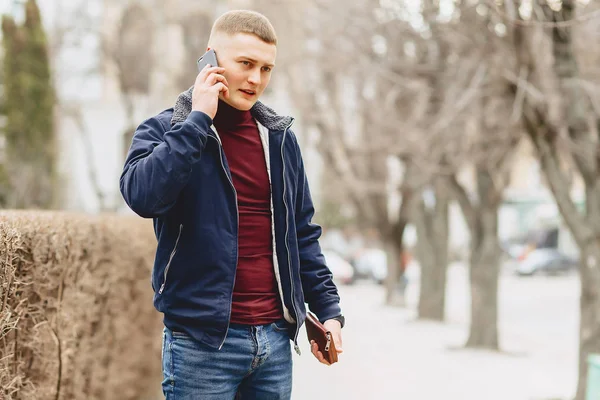 Sokak ortasında telefon ile basit ceketli çocuk duruyor