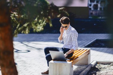 Telefon şık genç adamla iş üstünde laptop Park'ta güneşli günde