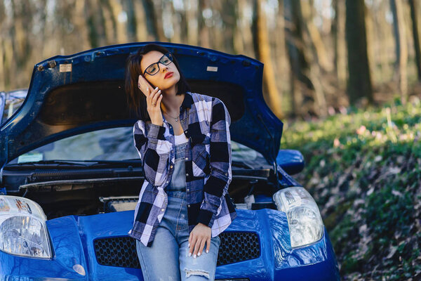 attractive girl with phone near open hood of car on road