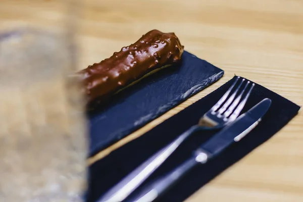 delicious chocolate eclair with a fork and a knife on a wooden table