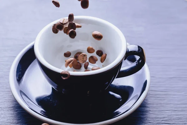 coffee beans falling to cup at black stone background