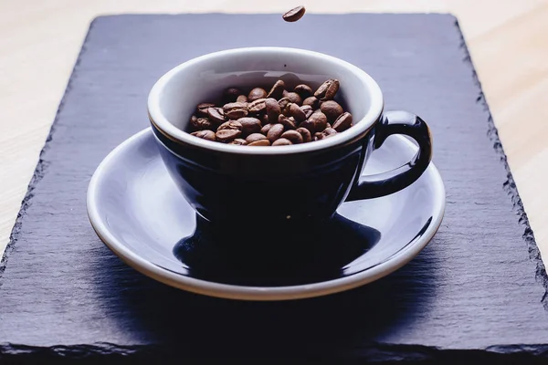 coffee beans falling to cup at black stone background