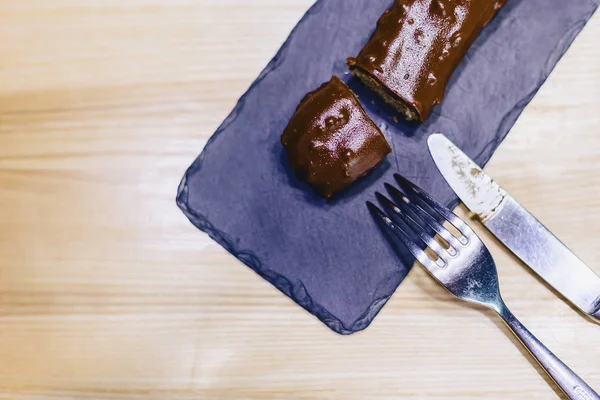 delicious chocolate eclair with a fork and a knife on a wooden table