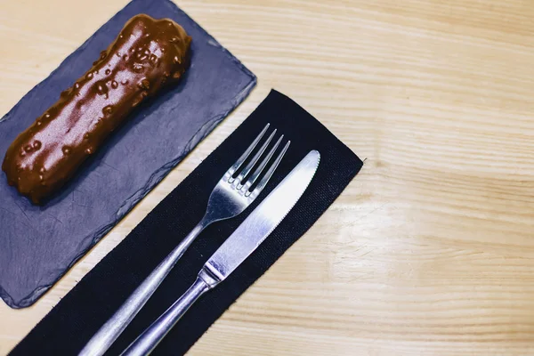 delicious chocolate eclair with a fork and a knife on a wooden table