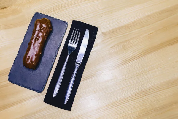 delicious chocolate eclair with a fork and a knife on a wooden table