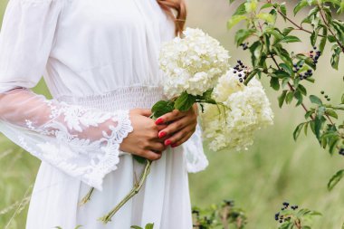 Genç güzel kız ile hafif soyunma yürüyüş Lawn yeşil yaz forest yakınındaki ellerinde çiçek