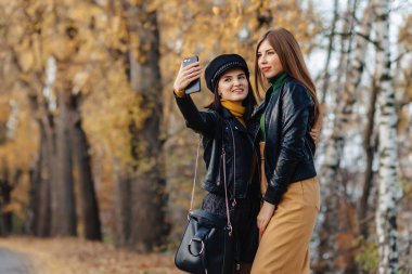 iki rahat gülümseyen genç kız sonbahar park Road'da bir yapmak fotoğraflar yürümek.