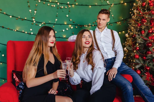 A young company of two girls and one guy celebrates a new year with glasses of champagne at home