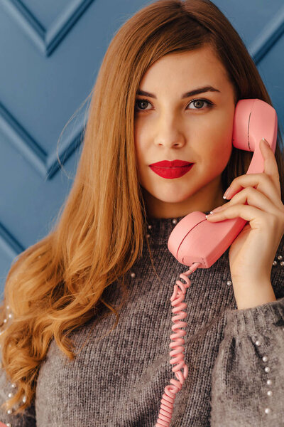 привлекательная стильная молодая девушка с ретро розовым телефоном на простых эмоциях аква-фона
