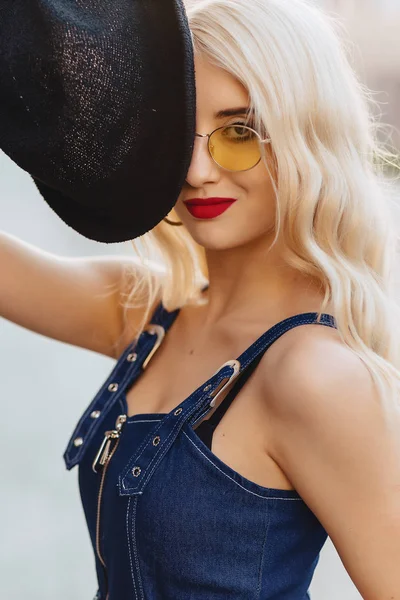 金发碧眼的女孩在太阳镜和时尚的帽子在温暖的夏日阳光城市 — 图库照片