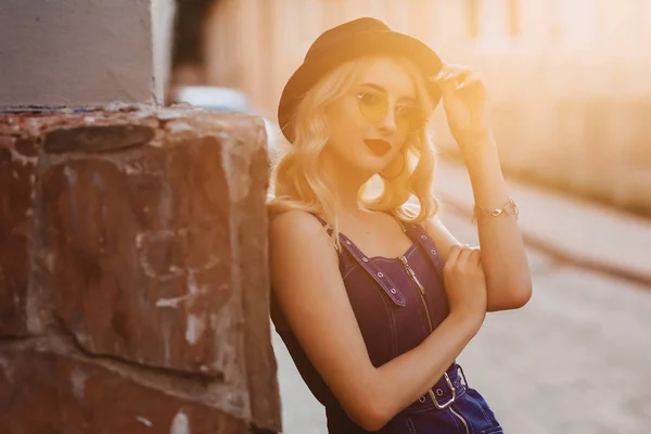 暖かい夏の日差しの都市でスタイリッシュな帽子とサングラスで魅力的なブロンドの女の子 — ストック写真