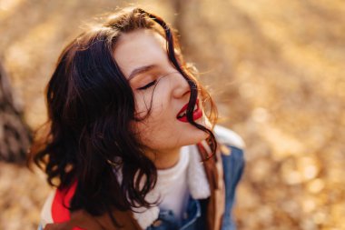 Genç güzel kız kırmızı dudaklı ve denim ceket kısa saç sonbahar güneşli şehirde yürür