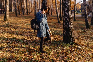 Genç güzel kız bir kot ceket sonbahar güneşli parkta yürüyor
